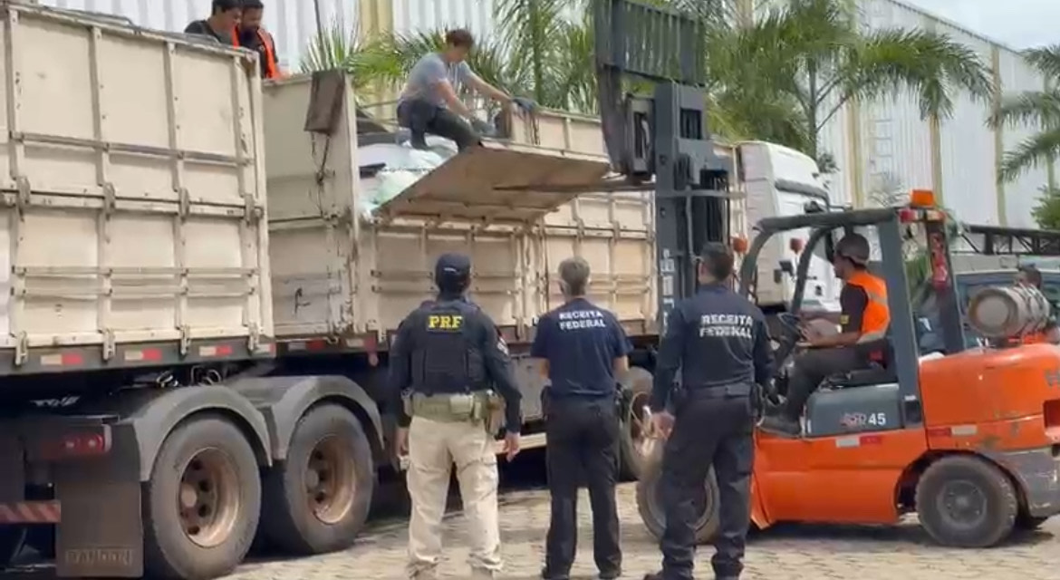 Imagem carga em caminhão sendo retirada pessoas e policiais acompanham 
