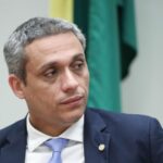 Imagem homem de terno escuro e gravata azul claro, olhando para o lado