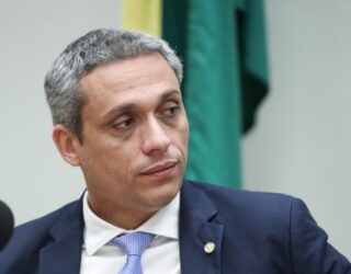 Imagem homem de terno escuro e gravata azul claro, olhando para o lado