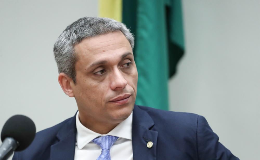 Imagem homem de terno escuro e gravata azul claro, olhando para o lado