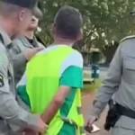 Imagem homem colete verde sendo conduzido pela policia