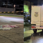 Imagem corpo caído no chão coberto, ao lado carro do Instituto médico legal