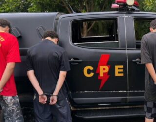 Imagem viatura da policia militar e três homens algemados