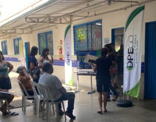 Imagem pessoas em pé e outras sentadas aguardando atendimento