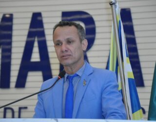 Imagem homem de terno azul falando ao microfone