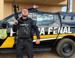 Imagem homem fardado com roupa preta segurando uma arma