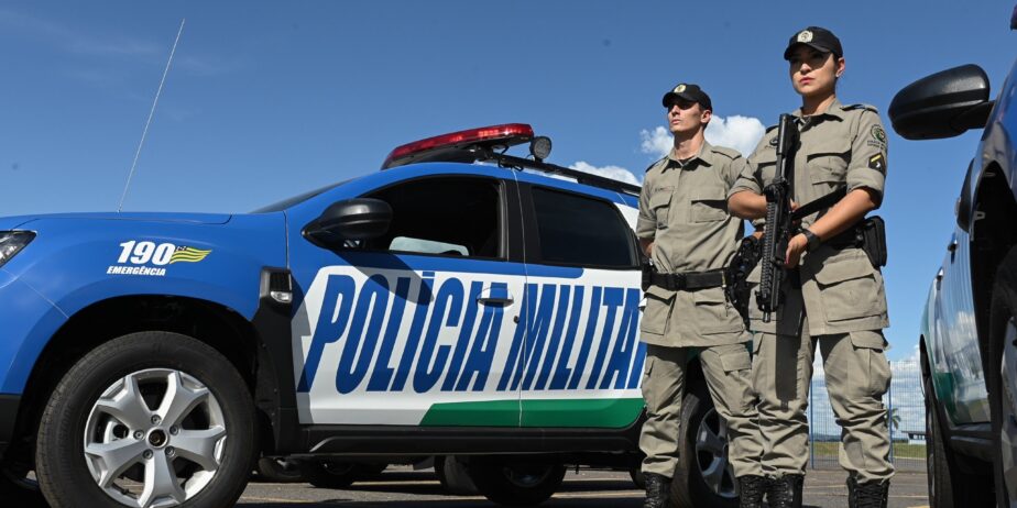 Imagem policiais militares e viatura ao fundo