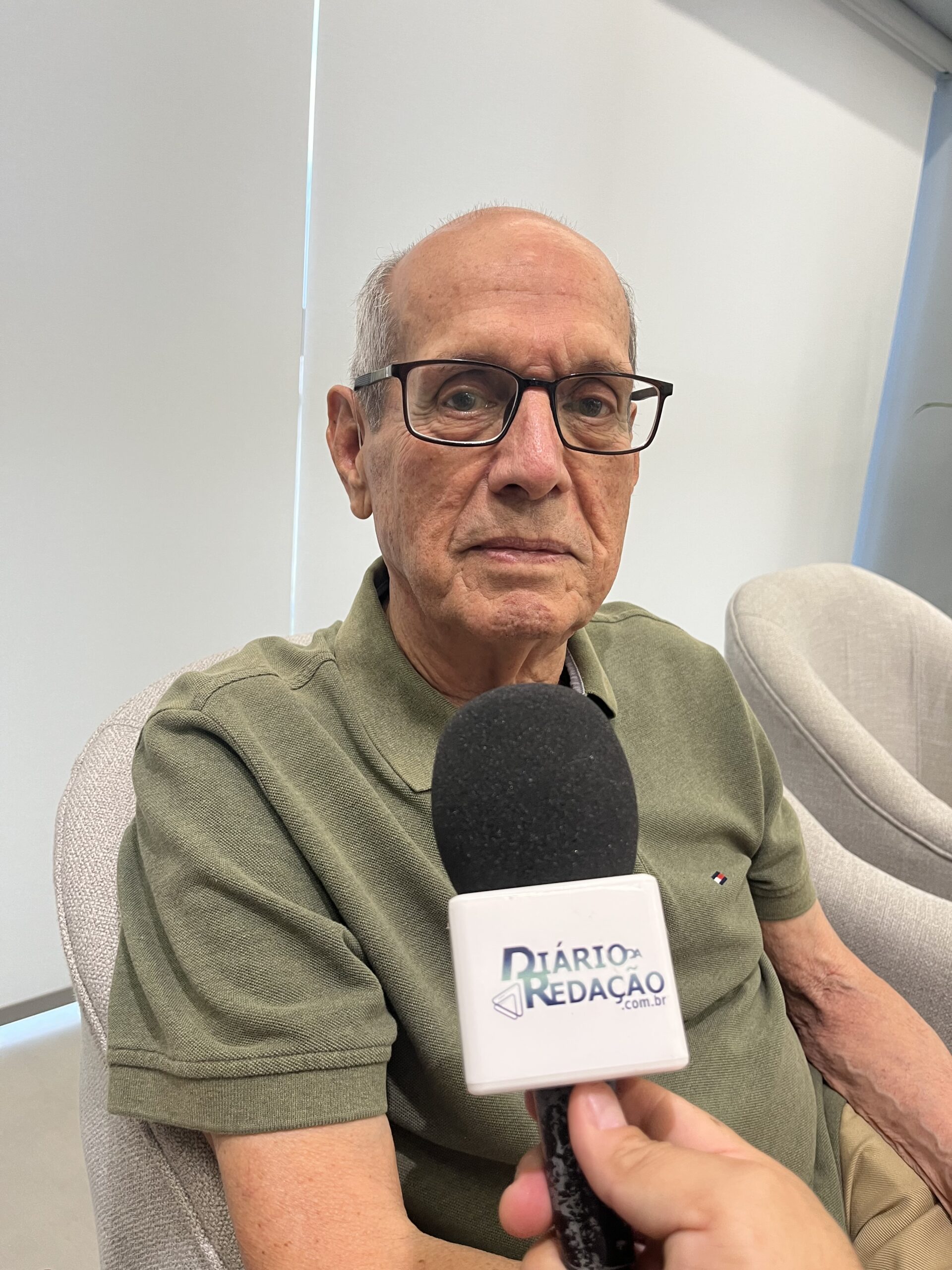 Imagem homem de óculos e camisa verde a frente um microfone