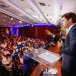 Imagem homem de terno falando para plateia lotada