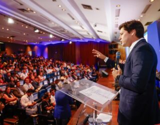 Imagem homem de terno falando para plateia lotada