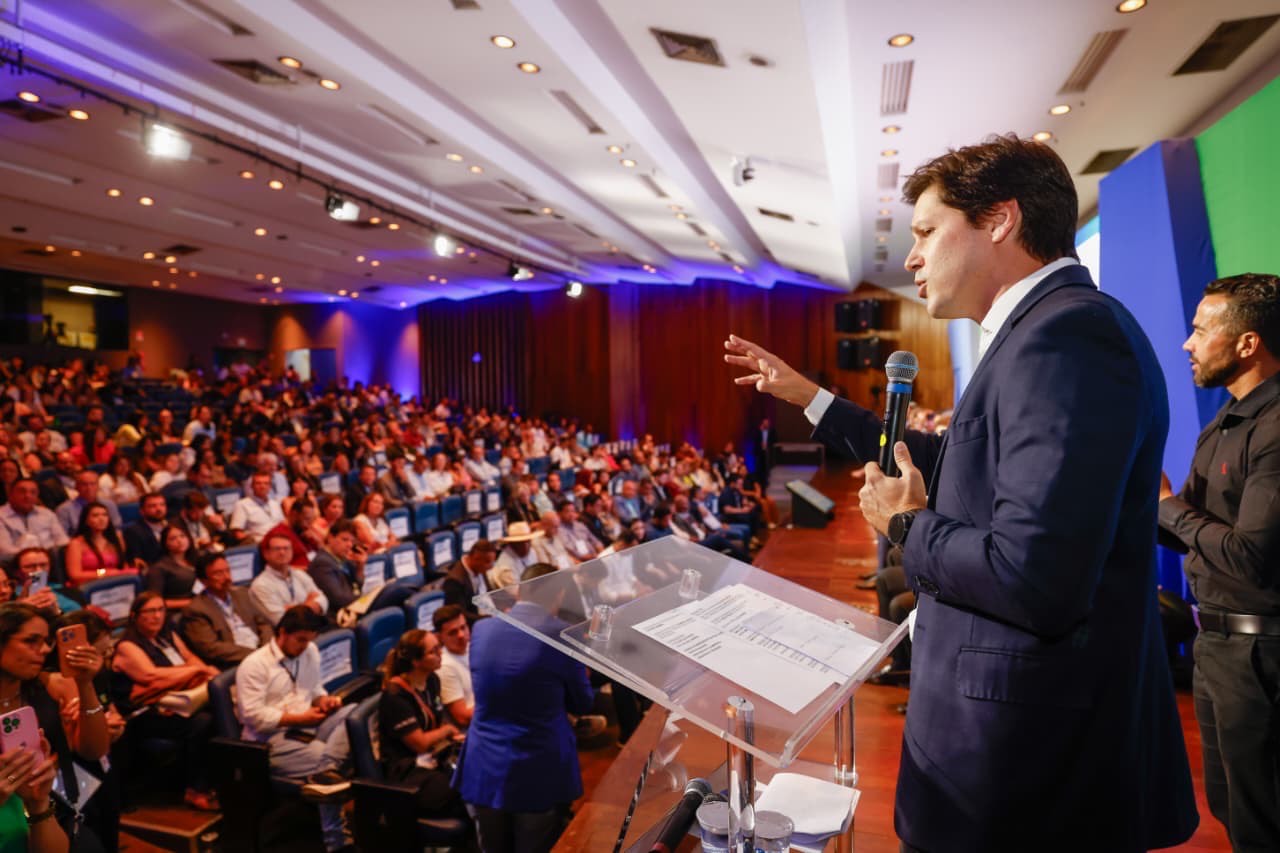 Imagem homem de terno falando para plateia lotada