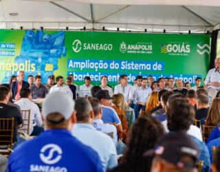 Imagem homem falando em microfone ao lado de várias pessoas no palco