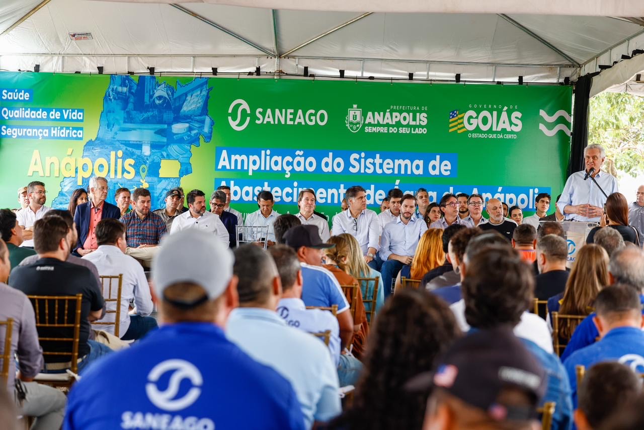 Imagem homem falando em microfone ao lado de várias pessoas no palco