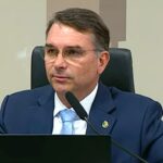 Imagem homem de terno e óculos falando ao microfone