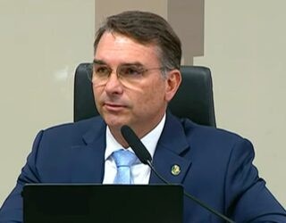 Imagem homem de terno e óculos falando ao microfone