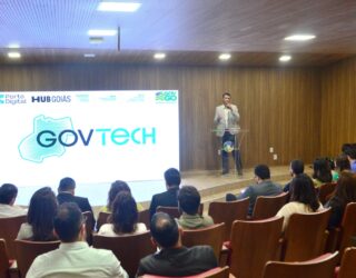 Imagem homem com microfone no palco falando para publico sentado