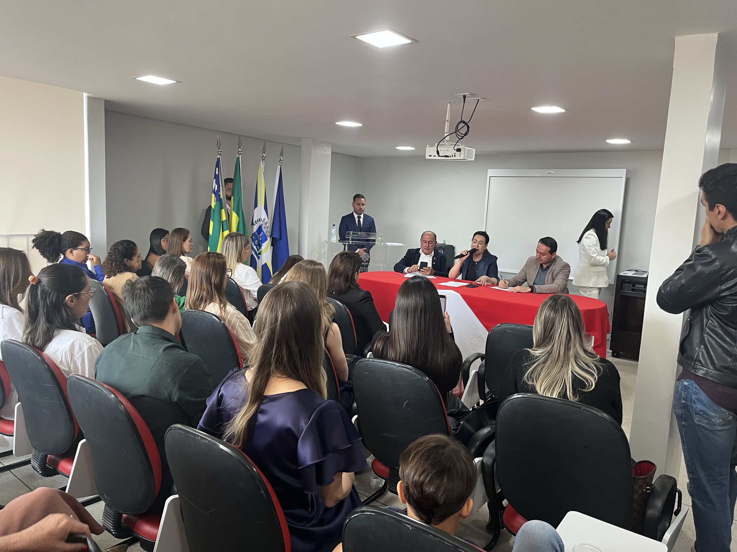 Imagem publico lota sala a frente três pessoas em uma mesa