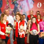 Imagem mulher segurando microfone de colete vermelho com pessoas ao redor