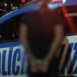 Imagem homem preso com mãos para traz em frente viatura da policia Militar