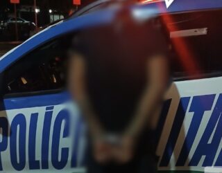 Imagem homem preso com mãos para traz em frente viatura da policia Militar