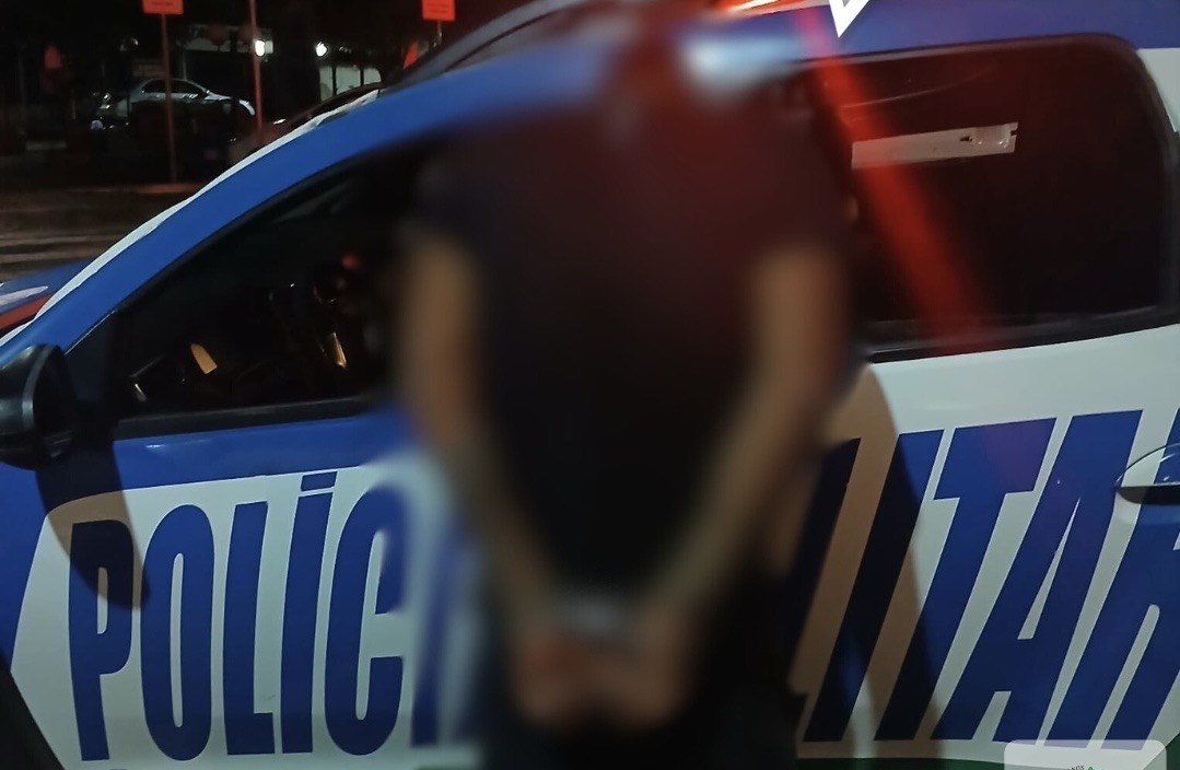 Imagem homem preso com mãos para traz em frente viatura da policia Militar