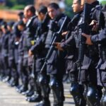 Imagem policiais militares de farda preta segurando arma longo
