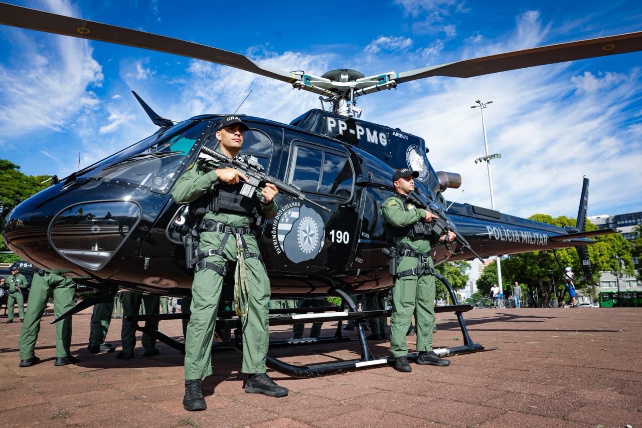 Imagem policiais militares armados em frente Helicóptero Polícia Militar de Goiás