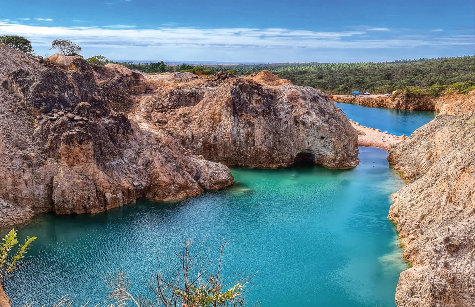 imagem retrata uma paisagem natural de grande impacto visual, formada por um lago de águas azul-esverdeadas intensas, encaixado entre paredões rochosos de tons terrosos e acinzentados. As rochas altas e irregulares mostram marcas evidentes de erosão e escavação, criando um cenári
