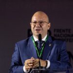 Imagem homem careca de terno falando ao microfone