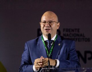 Imagem homem careca de terno falando ao microfone