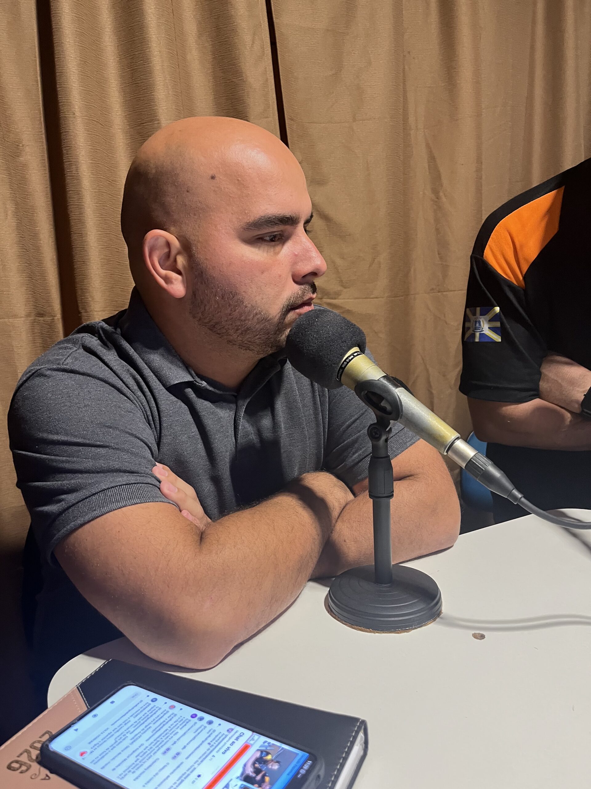 Imagem homem careca em frente o microfone de braços cruzados