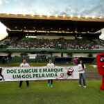 Imagem pessoas dentro de campo segurando faixa