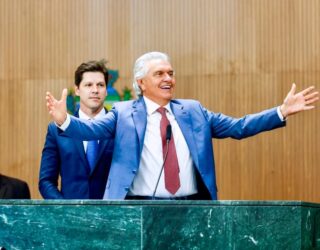 Imagem dois homens de terno um de braços abertos