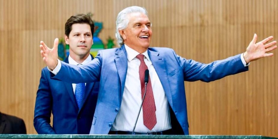 Imagem dois homens de terno um de braços abertos