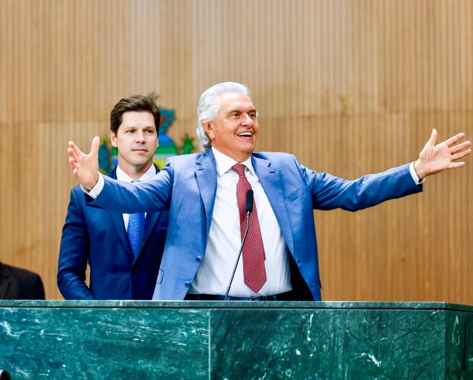 Imagem dois homens de terno um de braços abertos