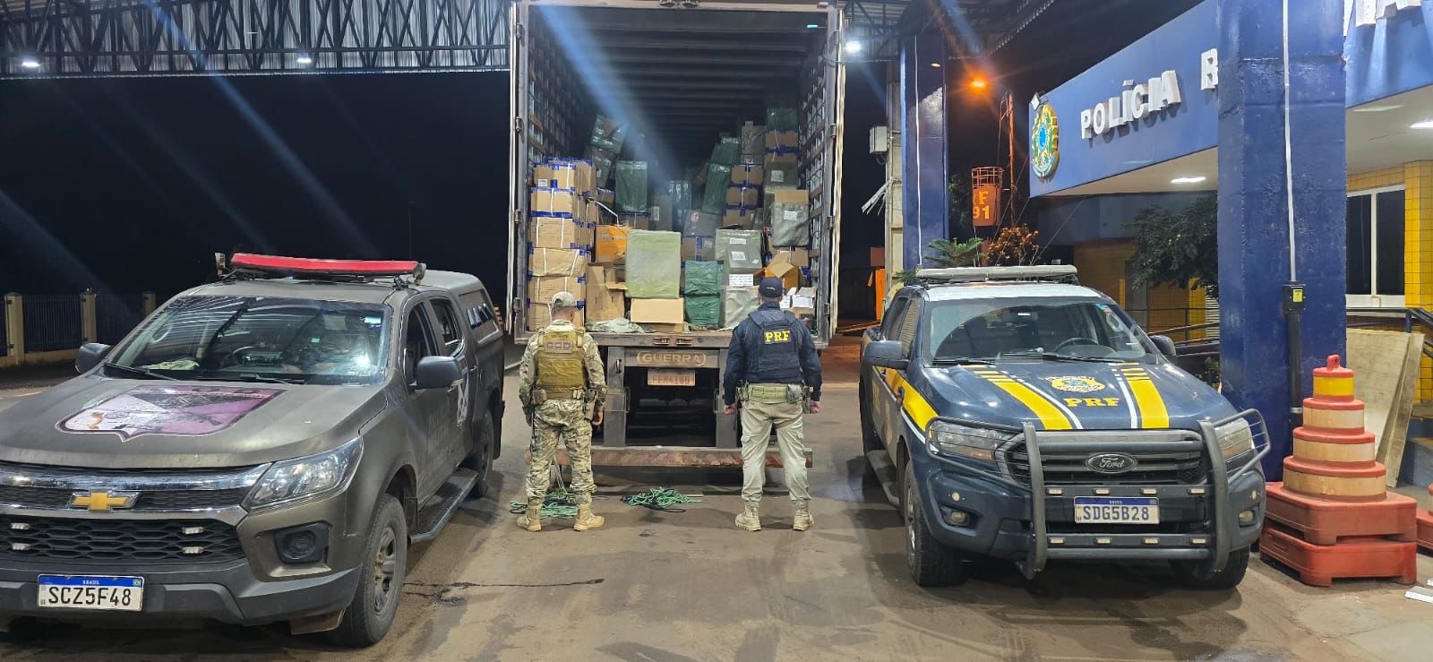Imagem policiais de costas, a frente caminhão baú aberto