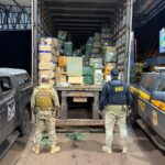 Imagem policiais de costas, a frente caminhão baú aberto