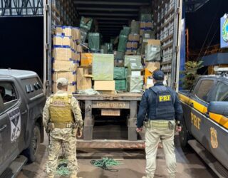 Imagem policiais de costas, a frente caminhão baú aberto