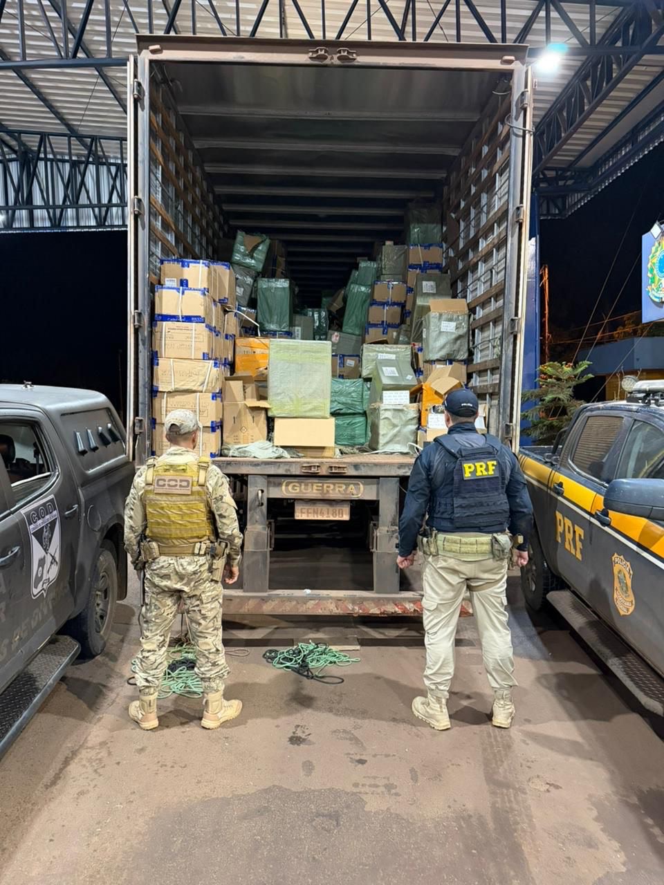 Imagem policiais de costas, a frente caminhão baú aberto