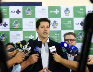 Imagem homem terno preto falando vários microfones