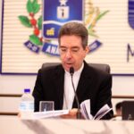 Imagem homem de terno preto sentado falando ao microfone