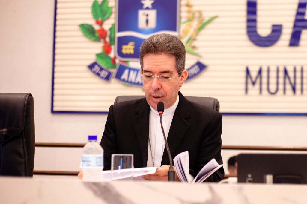 Imagem homem de terno preto sentado falando ao microfone