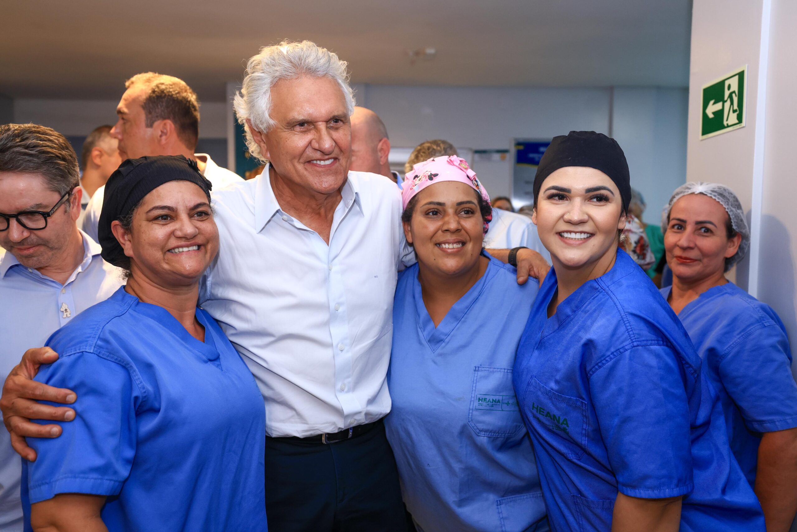 Imagem homem sorrindo abraçando mulheres de uniforme azul