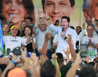 Imagem homem segurando microfone no palco ao lado de várias pessoas