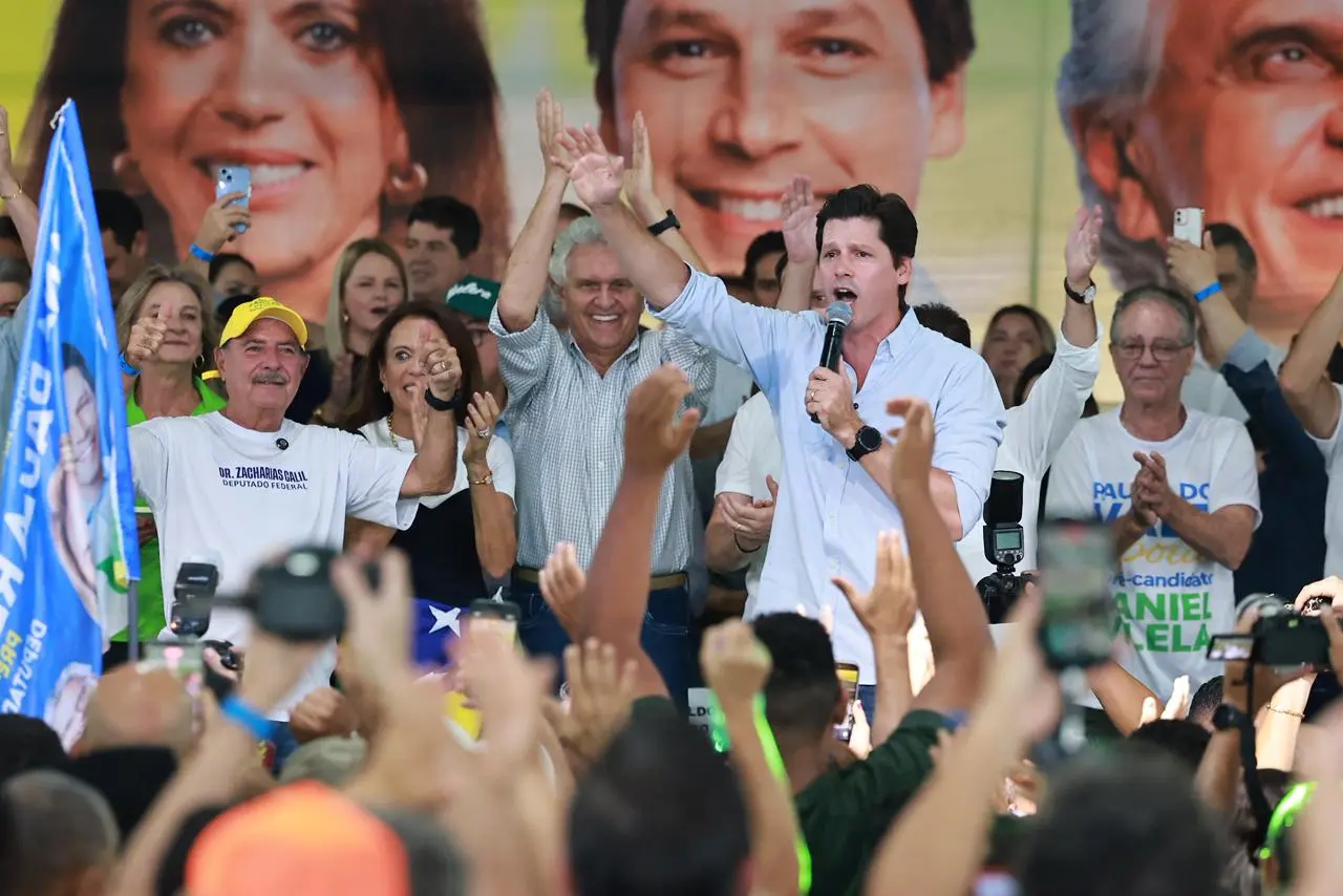 Imagem homem segurando microfone no palco ao lado de várias pessoas