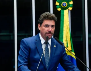 Imagem homem de terno e gravata falando ao microfone