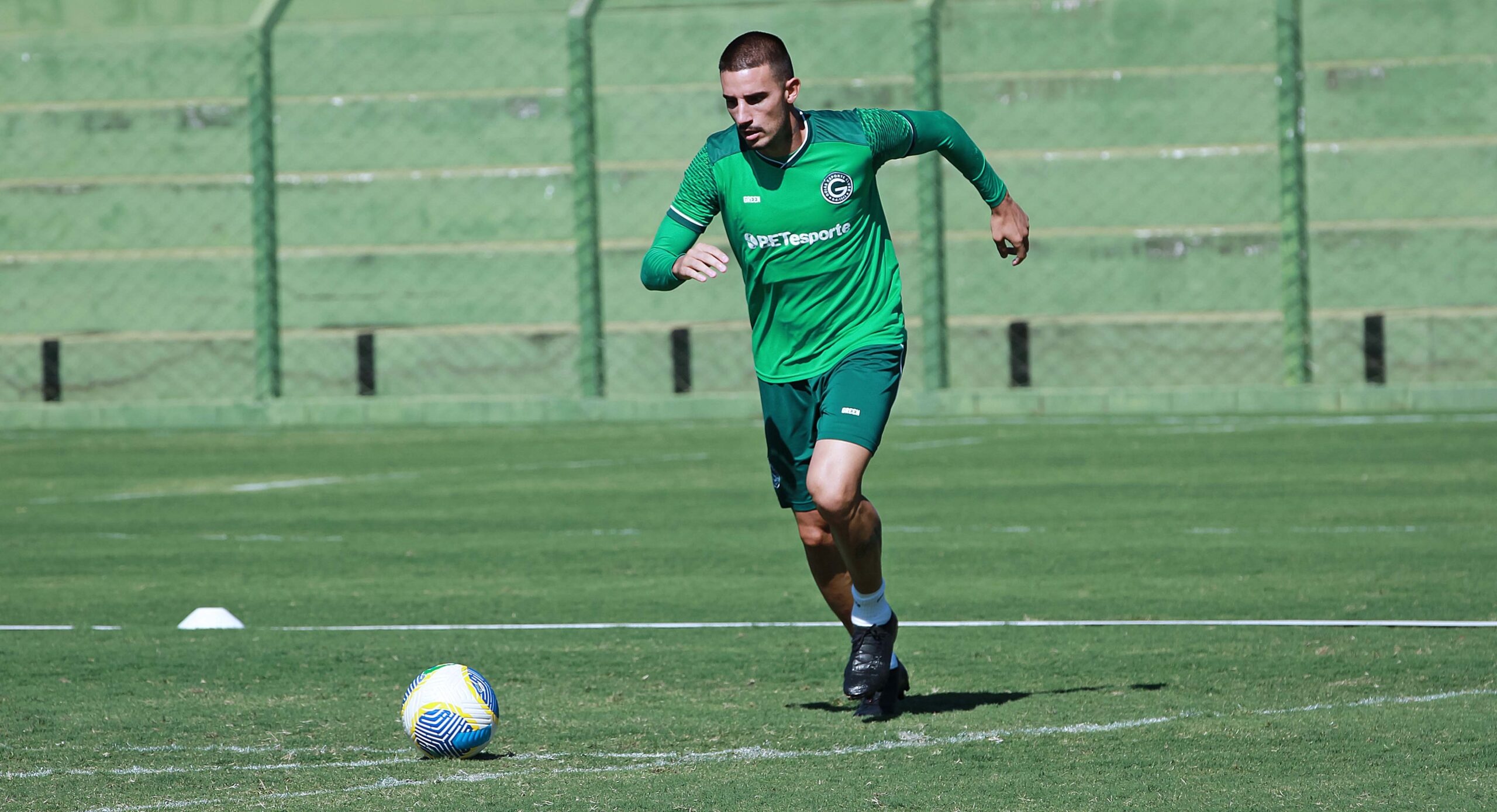 Imagem jogador de uniforme verde correndo com a bola no gramado