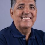 Imagem homem de braços cruzados e camisa azul sorrindo