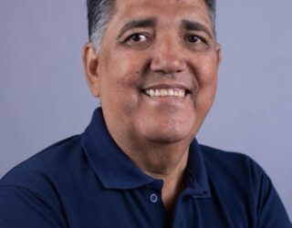 Imagem homem de braços cruzados e camisa azul sorrindo