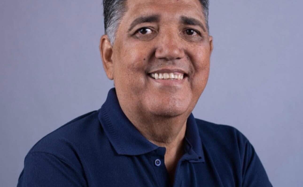 Imagem homem de braços cruzados e camisa azul sorrindo